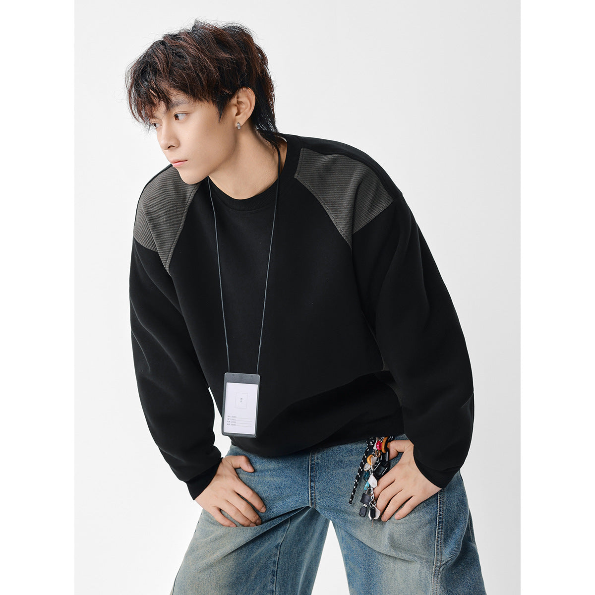 Model wearing an oversized black crewneck sweatshirt with textured charcoal shoulder panels.