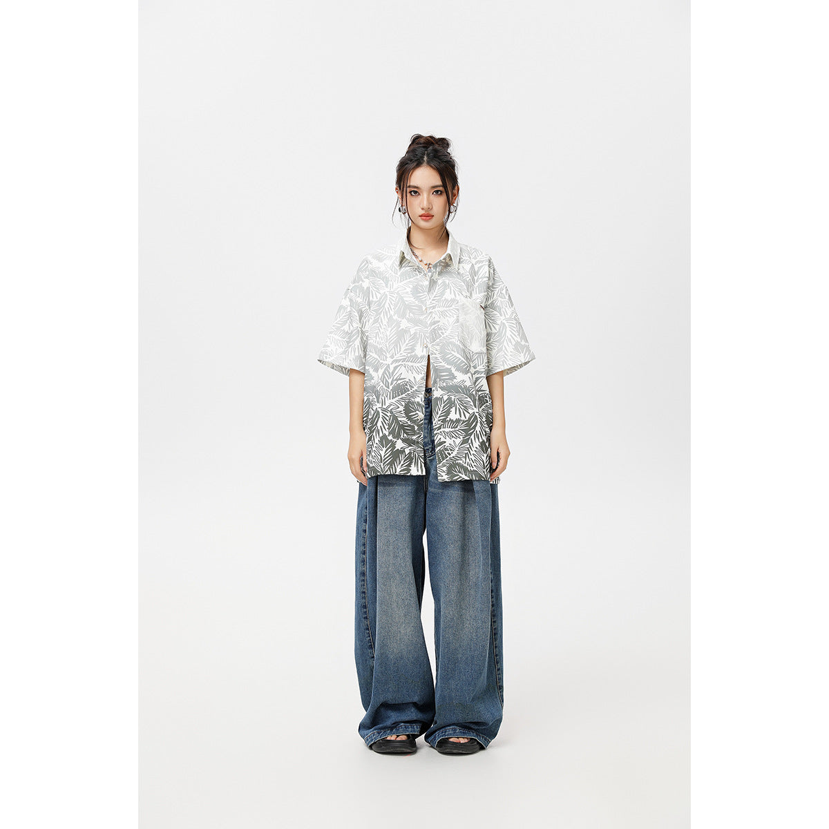 Model wearing a gray-and-white tropical leaf print short-sleeve button-up shirt with wide blue jeans, front view.