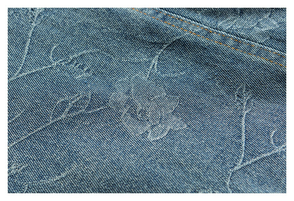 Close-up of blue denim with tonal stitched motifs and a line of orange topstitching.