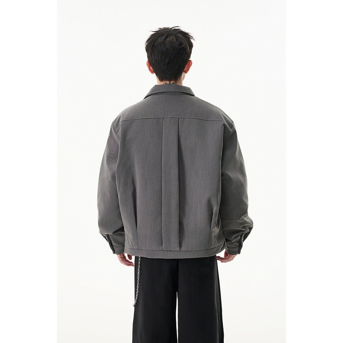 Back view of a model wearing a charcoal gray collared zip jacket with a center back pleat and black trousers.
