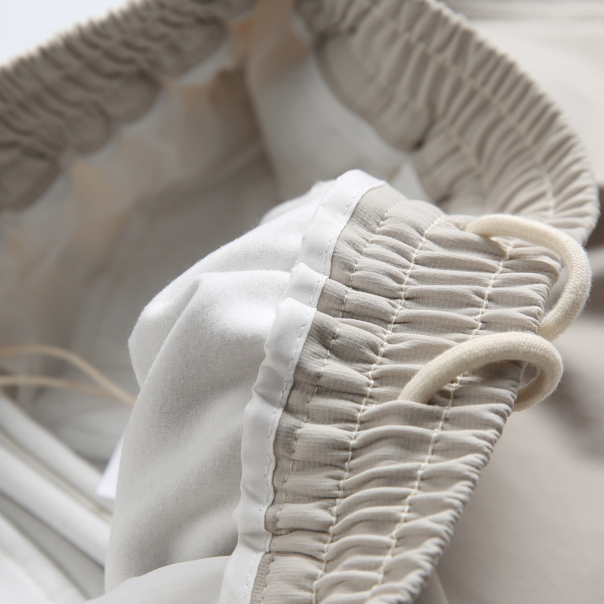Close-up of the inside of light beige trousers, showing the elastic waistband, drawcords and pale lining.
