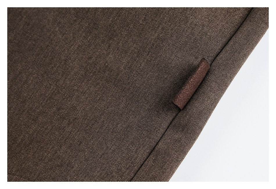 Close-up of dark brown woven fabric with a narrow brown tab beside a stitched edge.