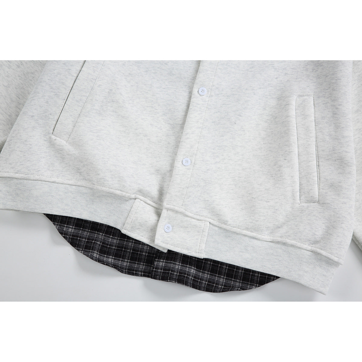 Close-up of the light gray jacket front with white buttons, welt pockets, ribbed hem, and plaid shirt-tail lining.
