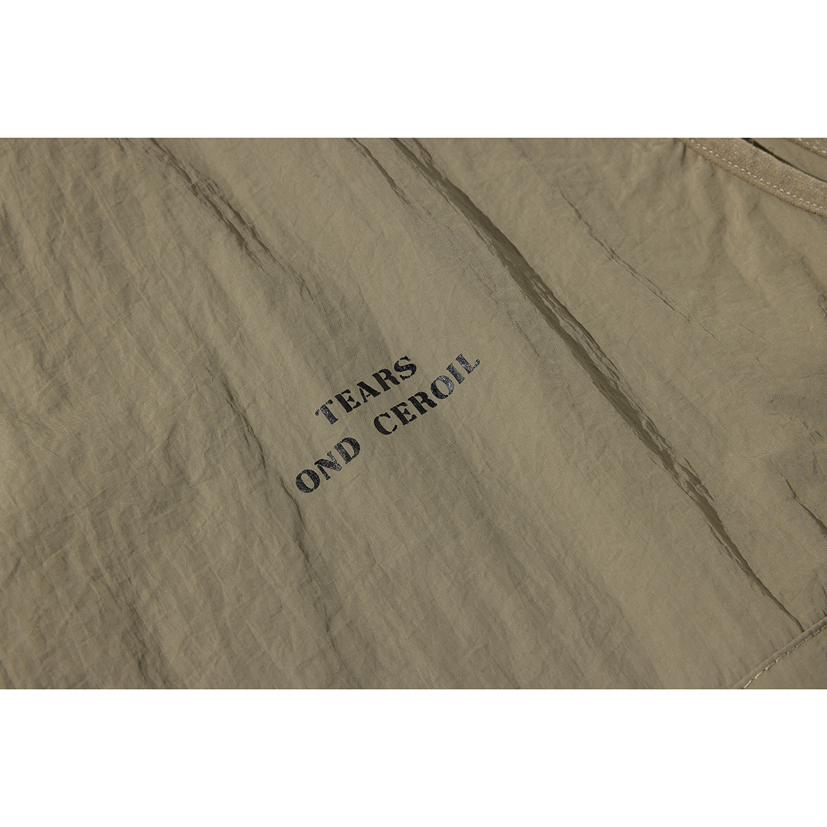 Close-up of small black English lettering printed on wrinkled olive-taupe fabric.