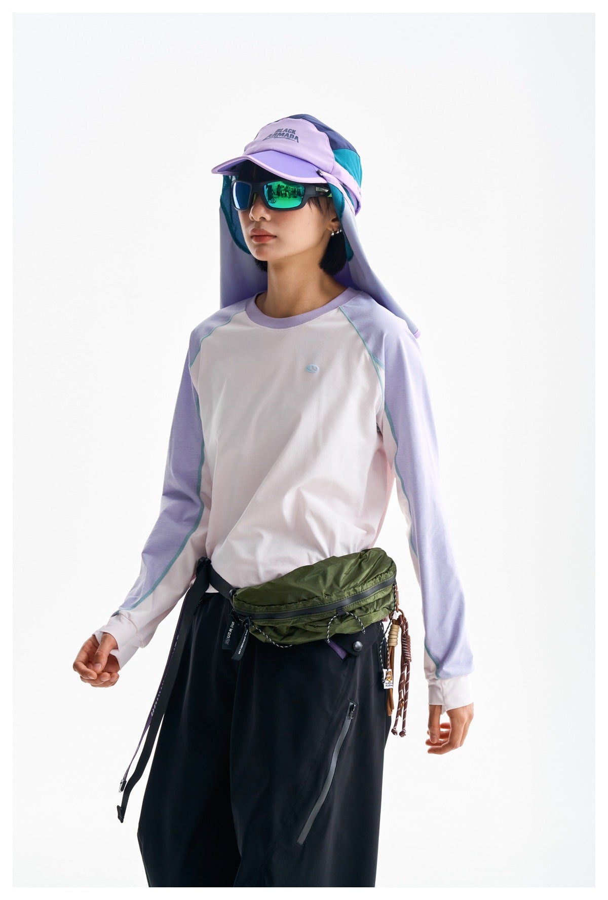 Three-quarter view of a woman wearing a white and lavender raglan top with black trousers and a green waist pack.