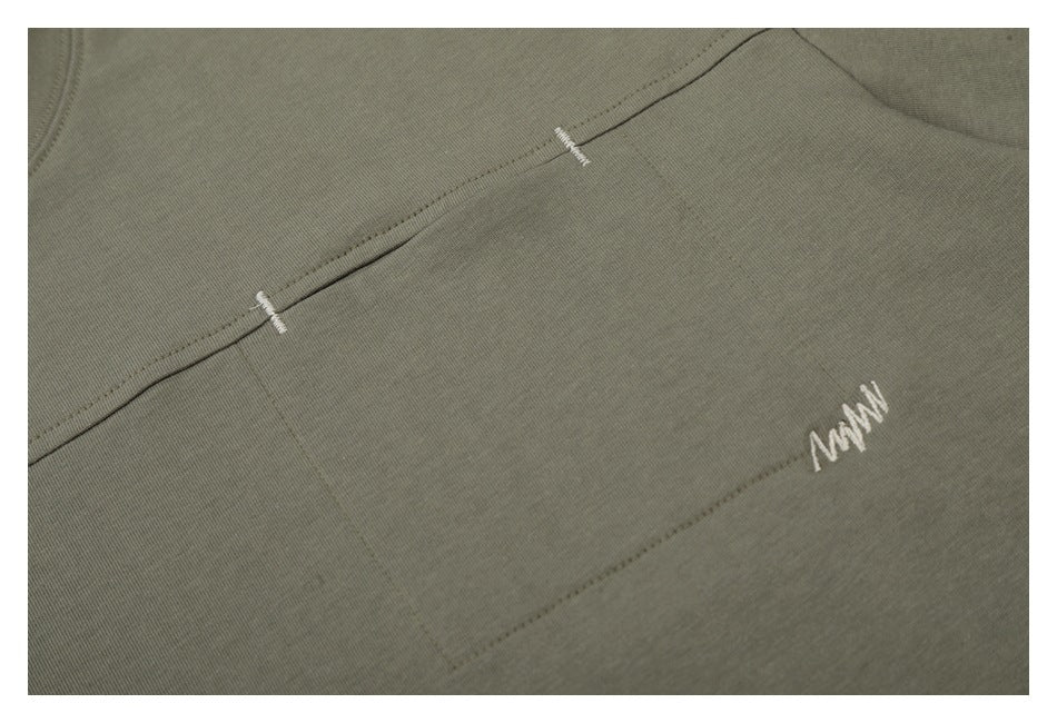 Close-up of an olive-gray garment with visible seams and a small white embroidered mark.