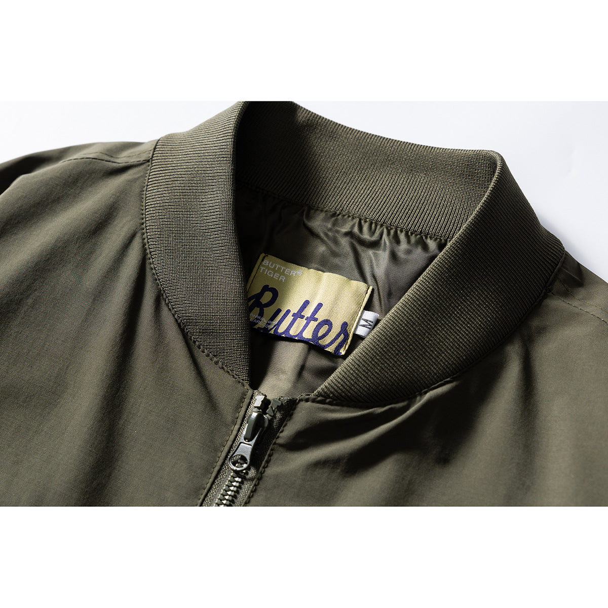 Close-up of an olive bomber jacket's ribbed collar, front zipper and sewn-in brand label.