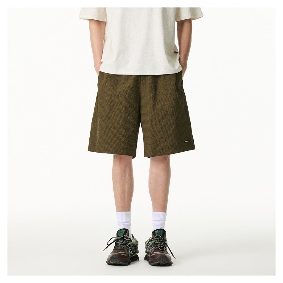 Front view of a model wearing olive textured knee-length shorts with a light T-shirt and sneakers.
