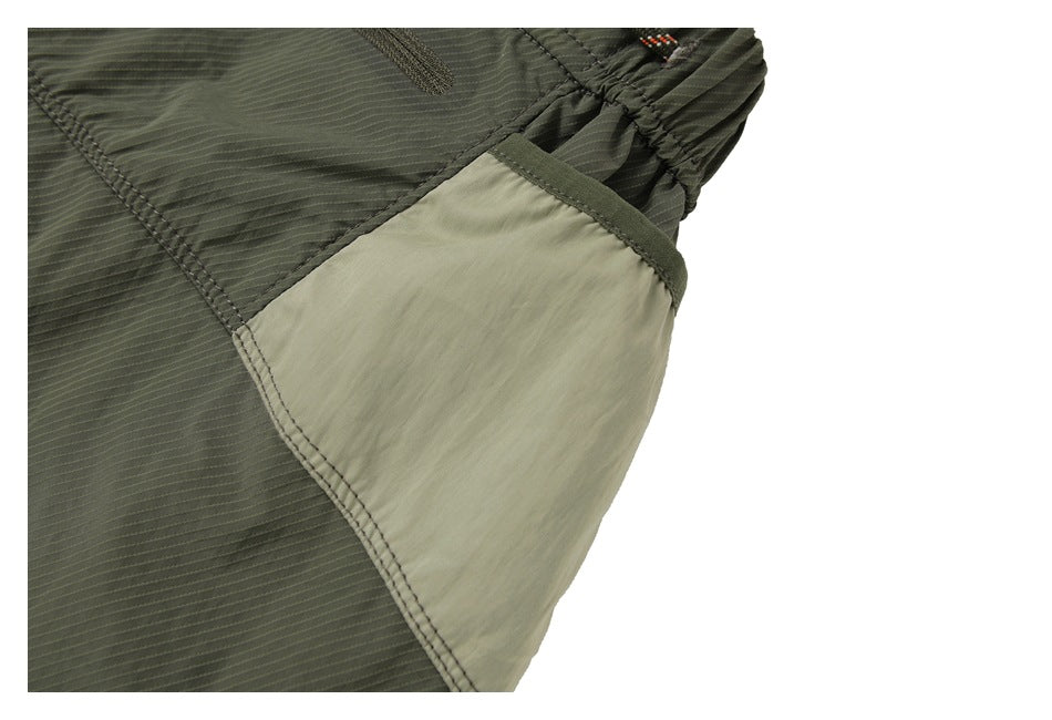 Close-up of an olive shorts leg with a pale contrast side panel and stitched seams.