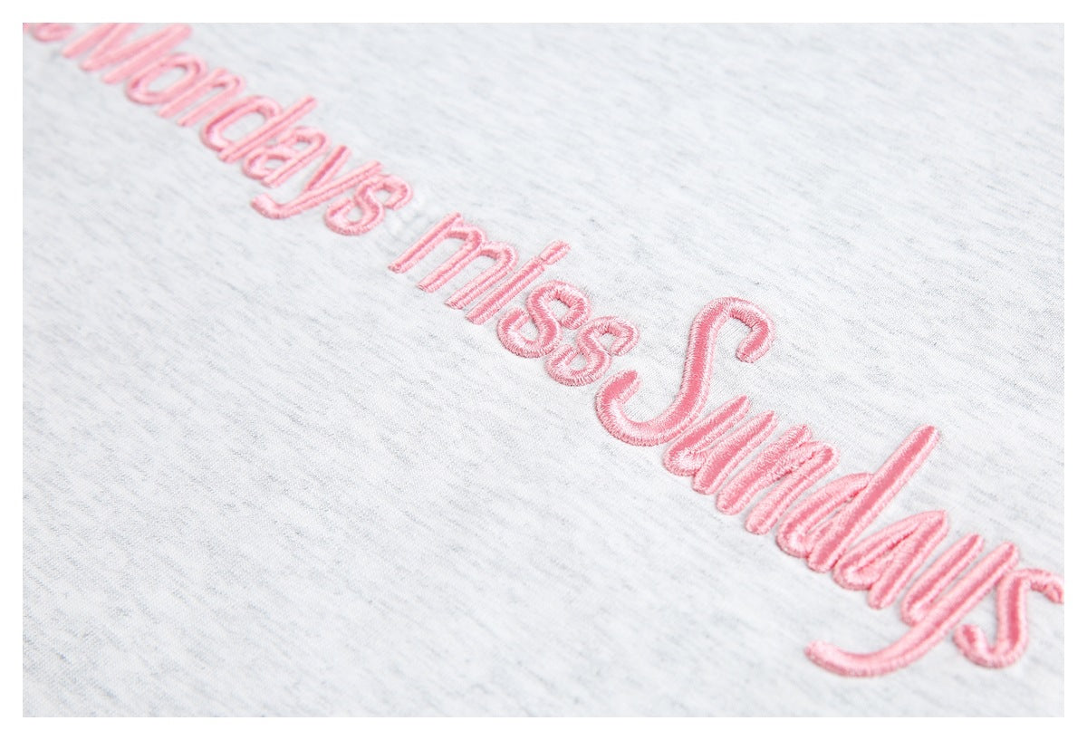 Tight close-up of raised pink “miss Sundays” embroidery on light gray heather fabric.