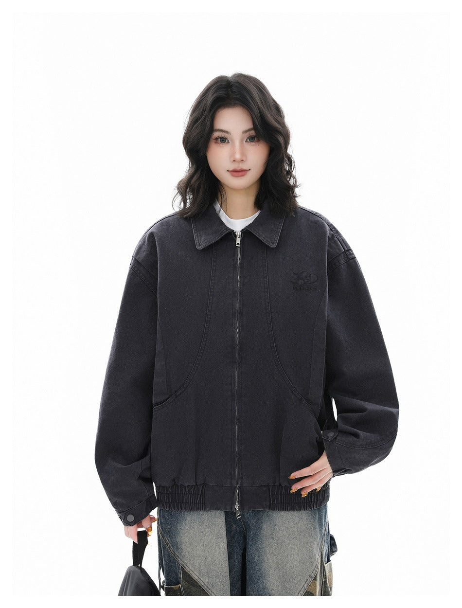 Model wearing a charcoal gray zip-front jacket over a white tee with faded jeans, holding a black bag