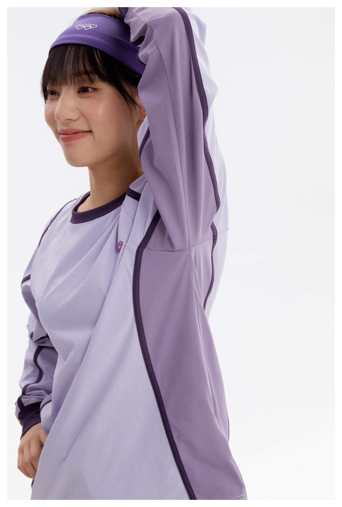 Side view of a model wearing a lavender long-sleeve top with dark purple piping and mesh side panels.