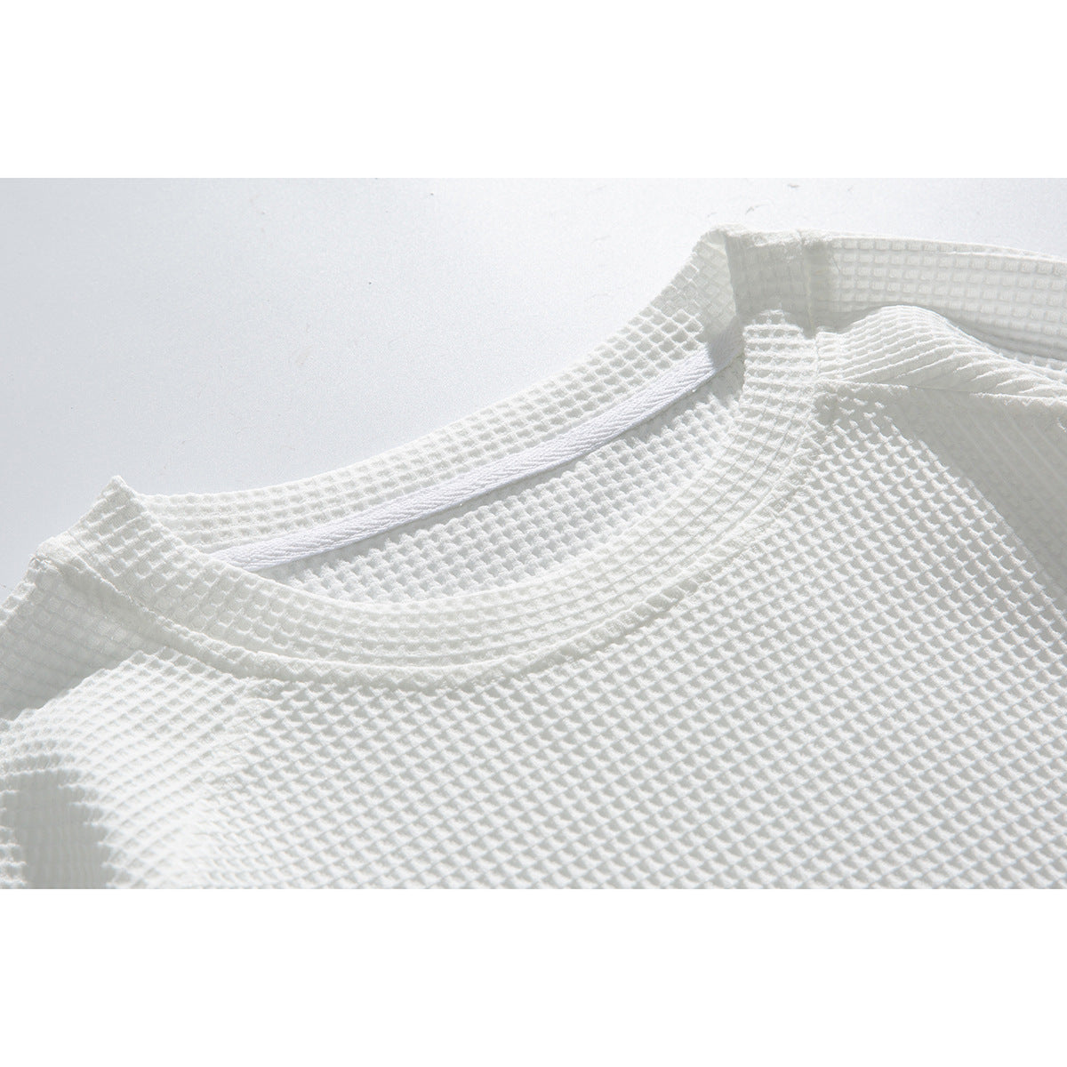 Close-up of a white textured shirt showing its crew neckline and waffle-knit surface.