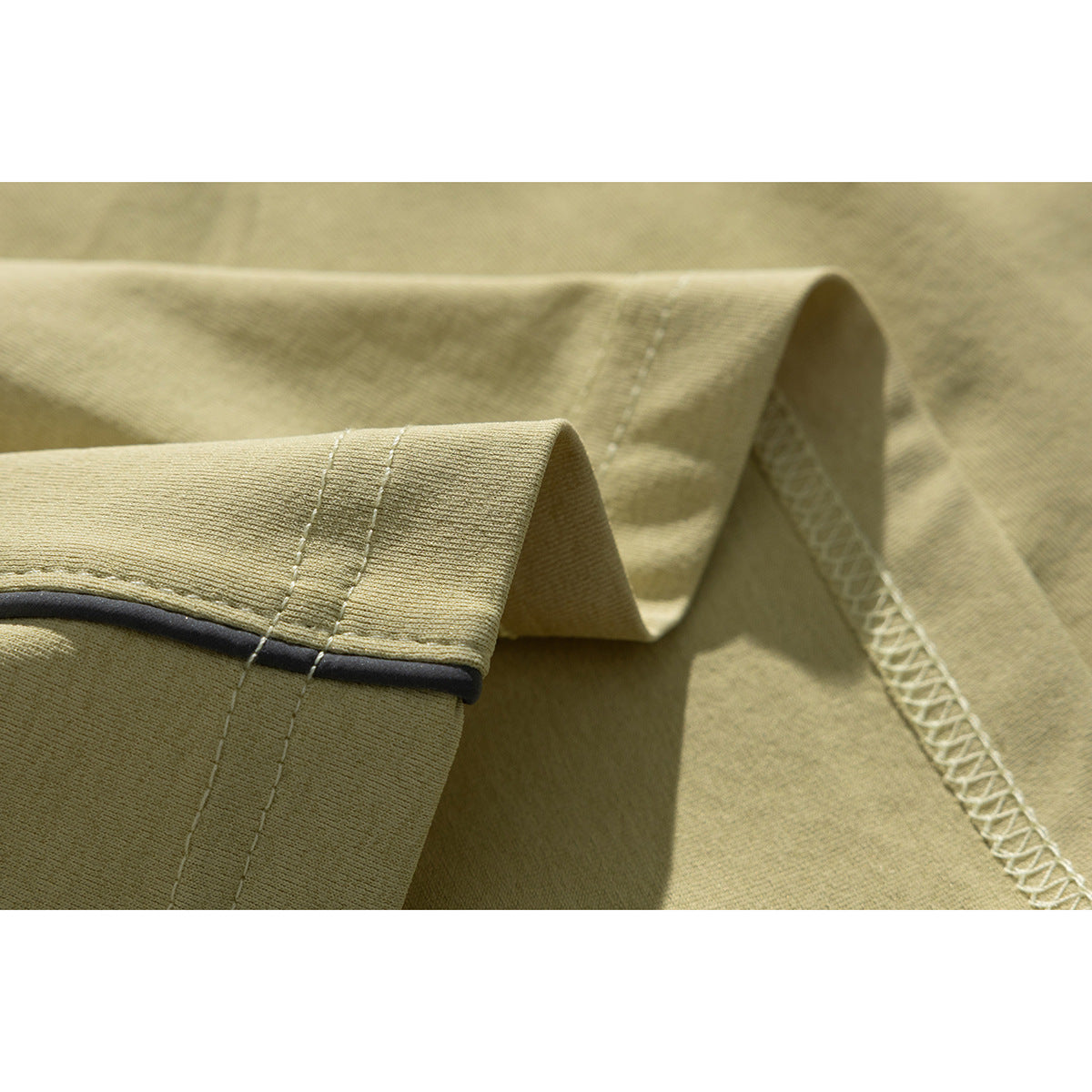 Close-up of a pale khaki T-shirt sleeve edge with dark piping and visible stitching.