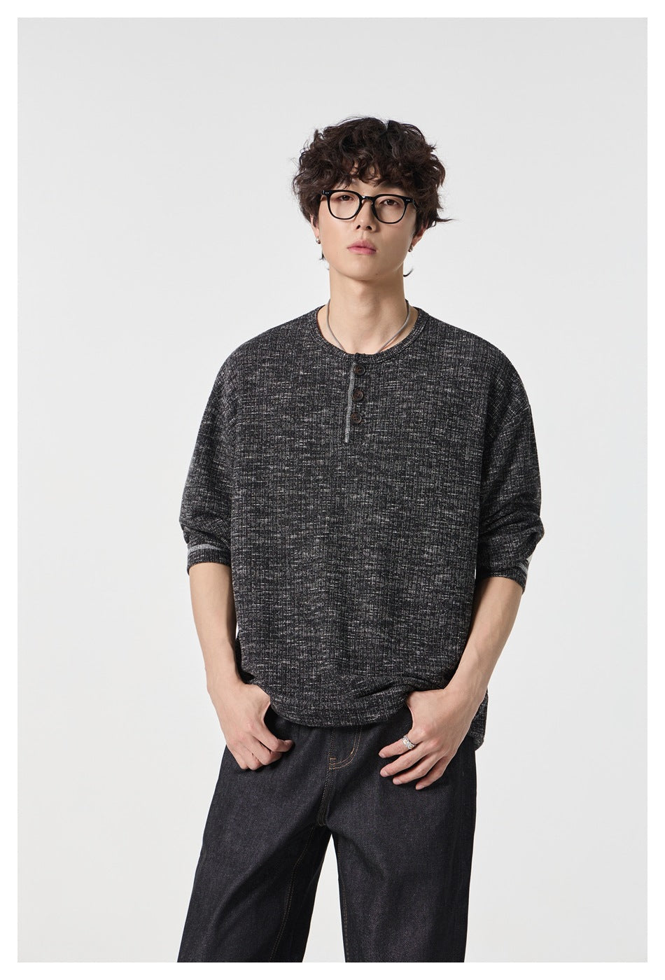 Man wearing a black heathered knit henley top with three buttons, hands in dark jeans pockets