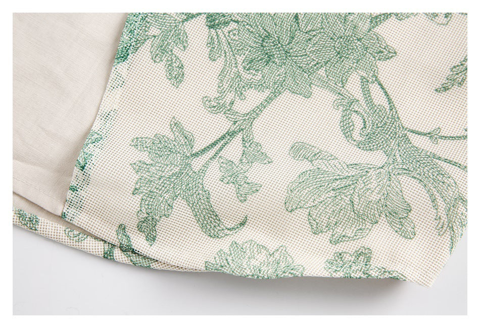 Close-up of green floral motifs on a cream grid-patterned fabric panel beside plain cream fabric.