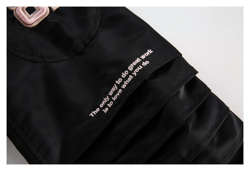 Close-up of a black jacket sleeve with a pale pink embroidered English quote and part of a pink patch.