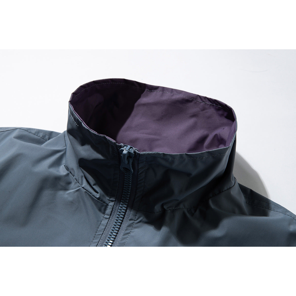 Close-up of a slate-blue jacket’s high collar, showing its purple lining and front zipper.