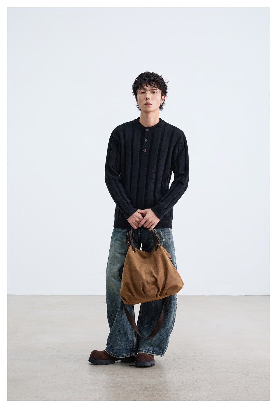 Model wearing black ribbed button-placket sweater with wide jeans, holding a brown bag, full-length front view