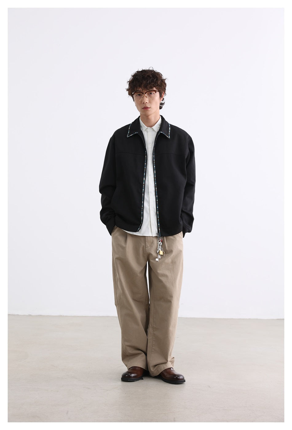 Full-length front view of a model wearing a black jacket with multicolor trim and loose beige trousers.