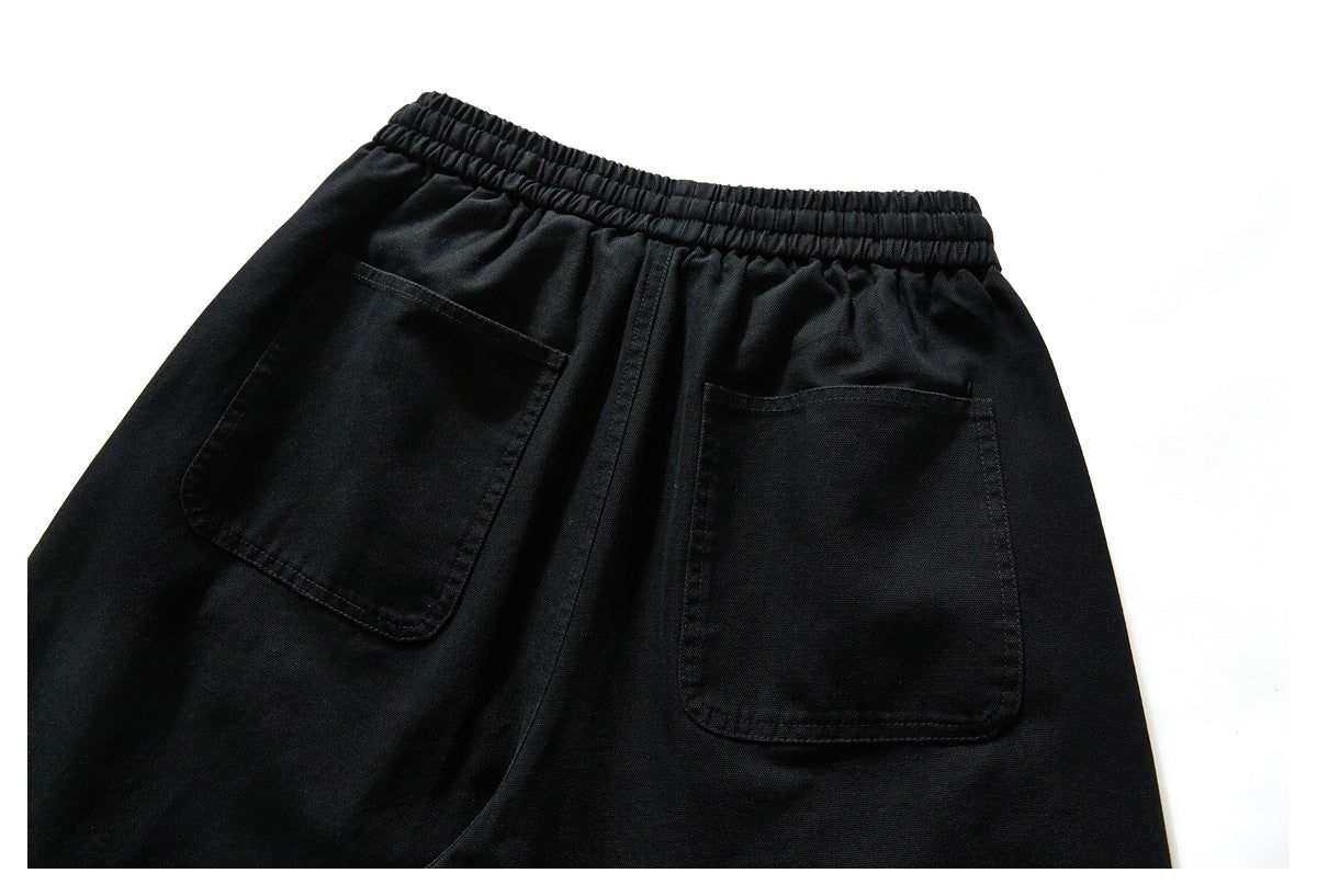 Close-up of the back of black pants, highlighting the elastic waistband and two patch pockets.