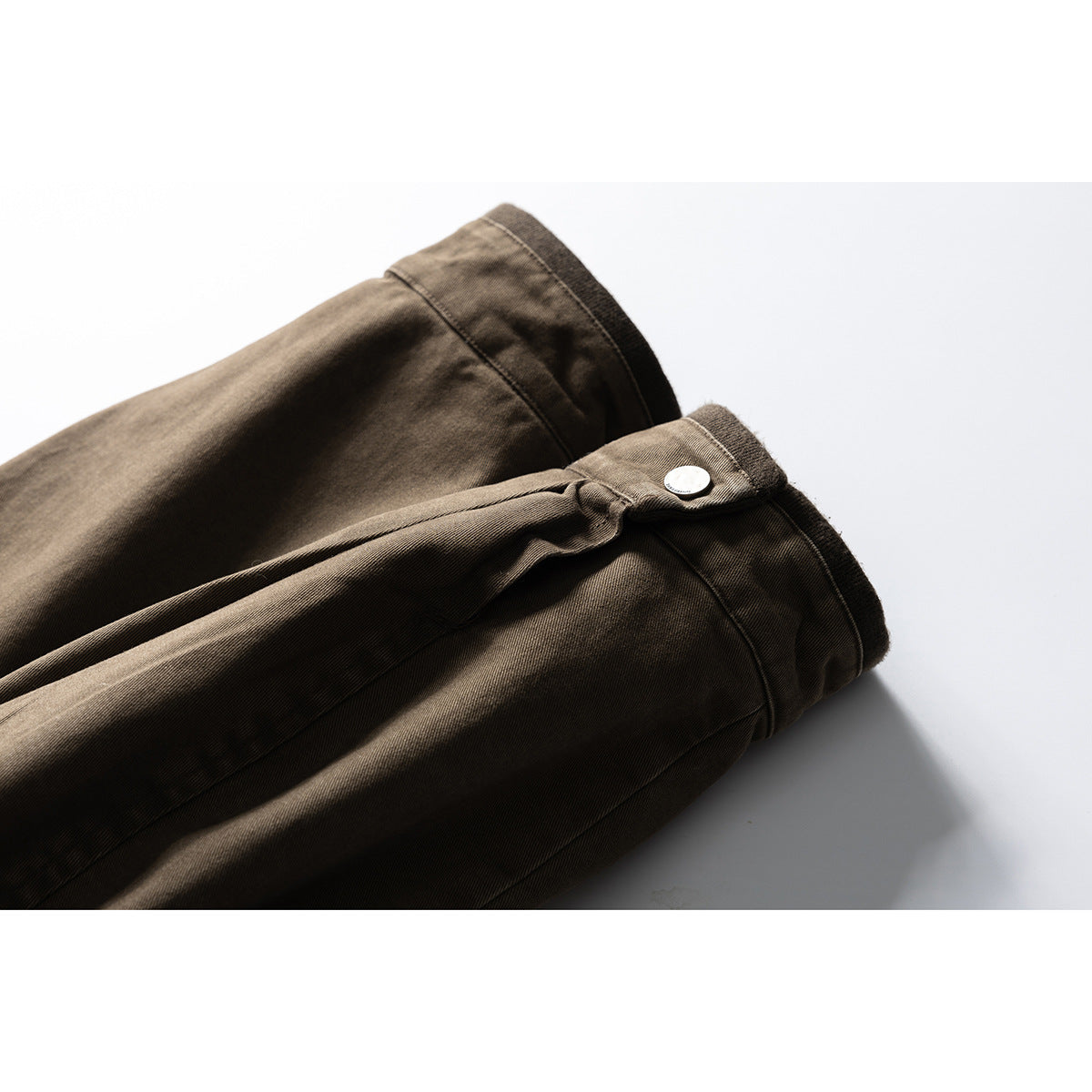 Close-up of the brown jacket's sleeve cuff with a buttoned tab and ribbed edge.