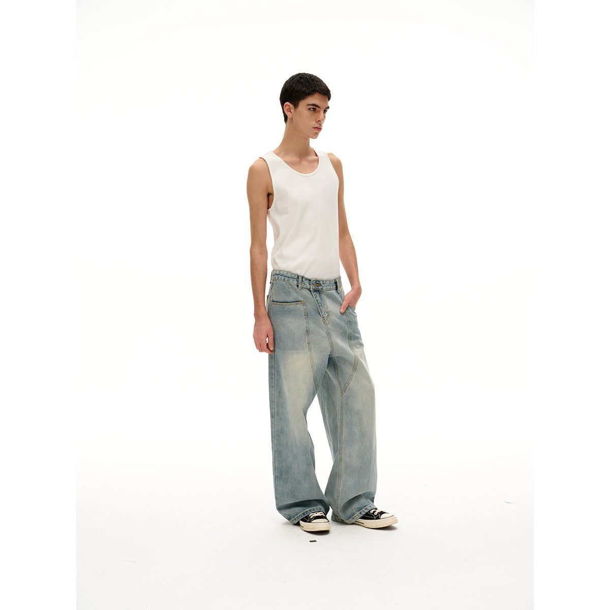 Model in a white tank top and oversized light-wash jeans, shown at a three-quarter angle with one hand in a pocket.