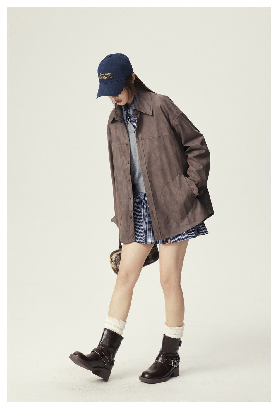 Model wearing a brown oversized button-front jacket with patch pockets over a checked skirt and layered top.