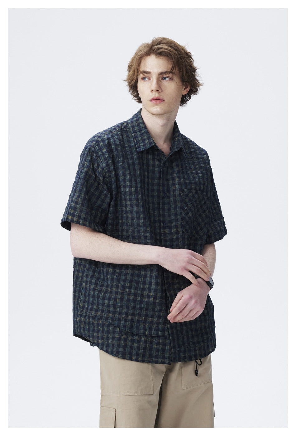 Model wearing a dark navy and green plaid short-sleeve button-up shirt, shown from a slight angle.