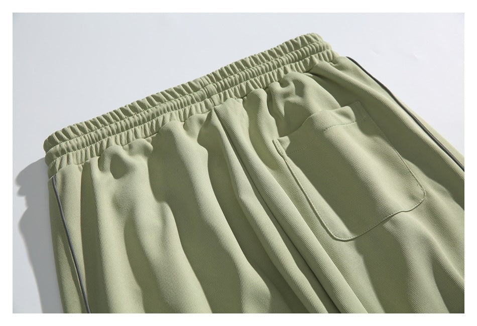 Sage green pants close-up showing the gathered elastic waistband, side piping, and a patch pocket.