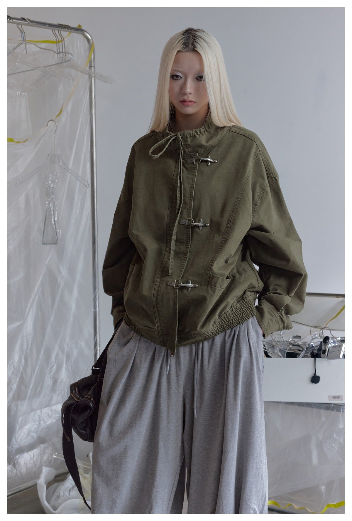 Model wearing an olive jacket with a gathered drawstring collar, silver hook closures, large pockets, and an elasticized hem.