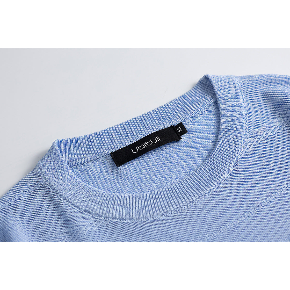 Close-up of a light blue knit shirt’s ribbed crew neck and interior brand label.