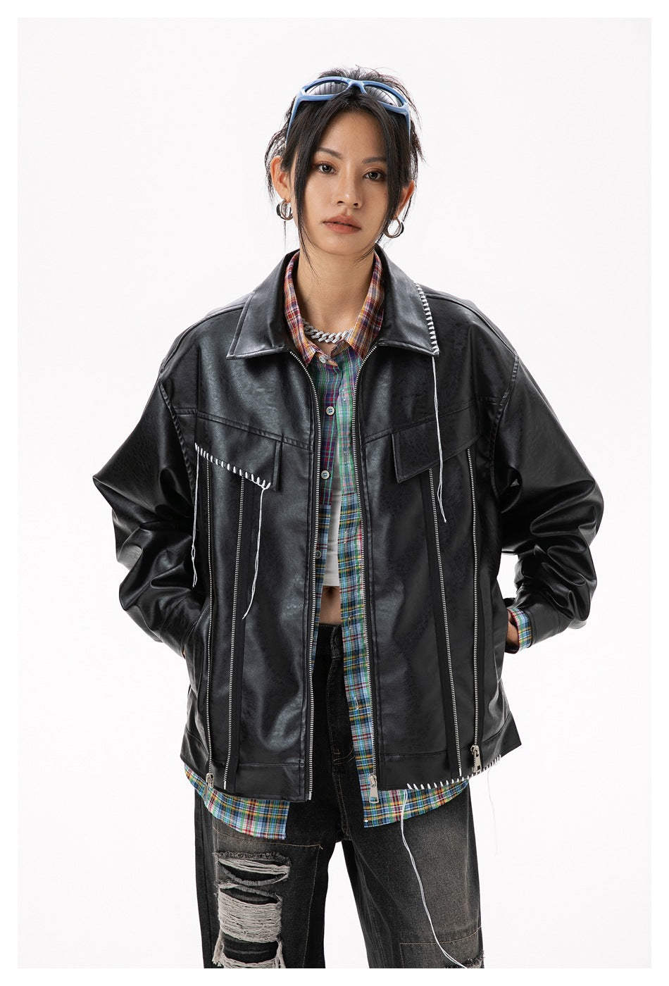 Close view of a model wearing a black jacket with plaid lining, white contrast stitching, and multiple zippers.