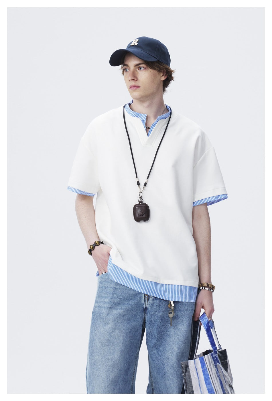 Model wearing an oversized white V-neck short-sleeve tee over a blue-and-white striped shirt with jeans.