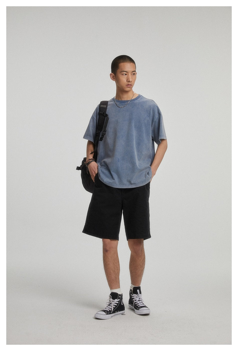 Model wearing an oversized faded blue T-shirt and black shorts against a plain studio backdrop.
