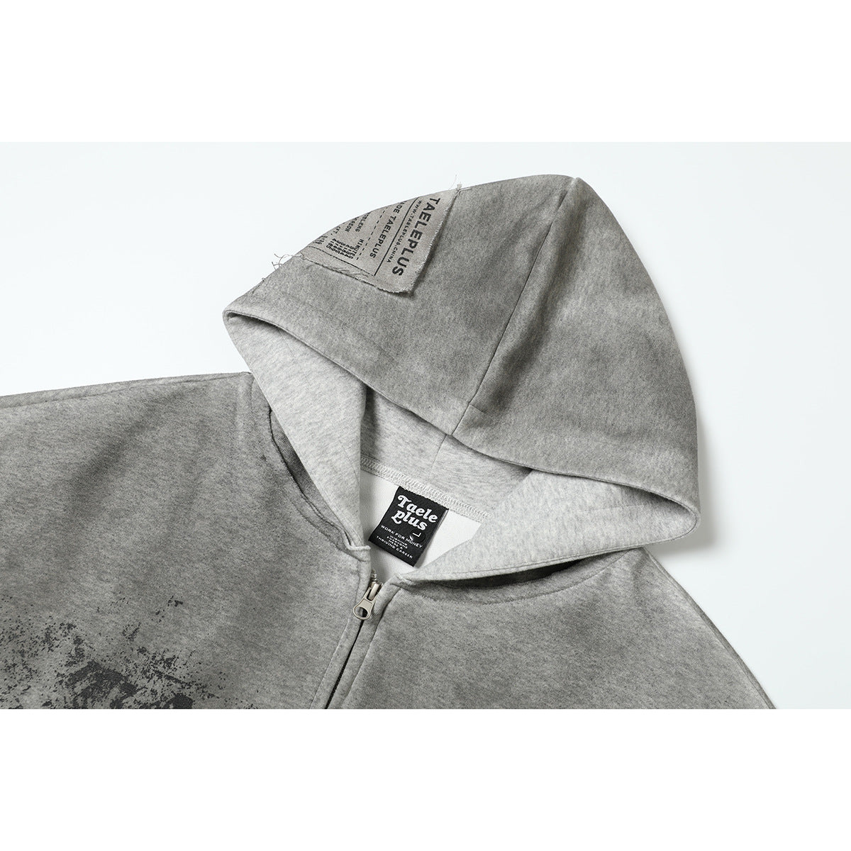 Close-up of a gray zip-up hoodie showing its hood, sewn labels, zipper, and distressed black print.