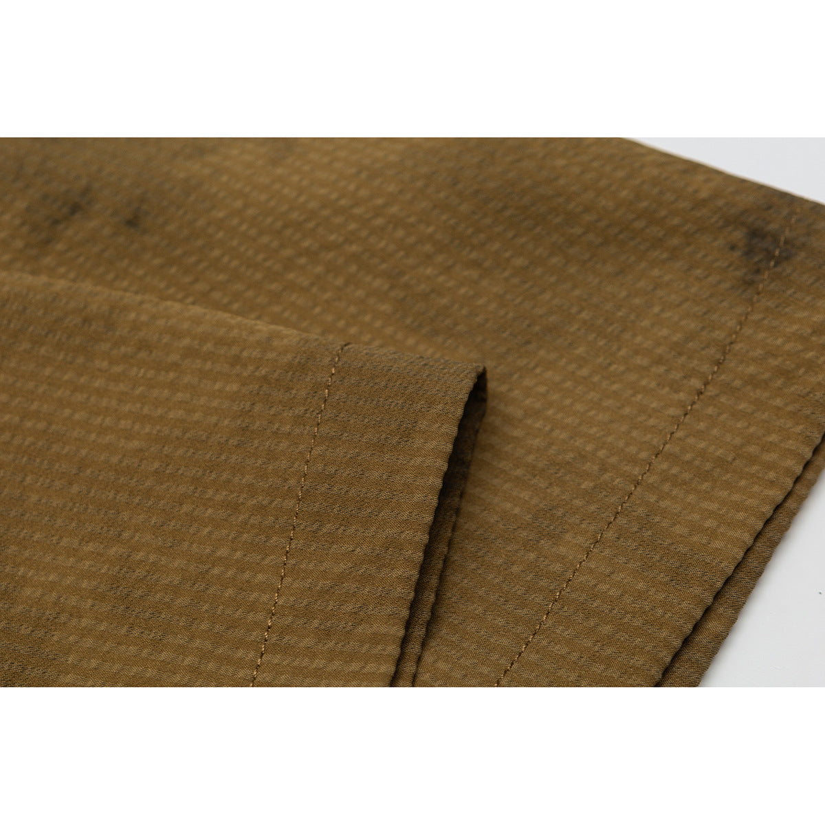 Close-up of brown textured shirt fabric, a folded edge, and parallel stitched seams.