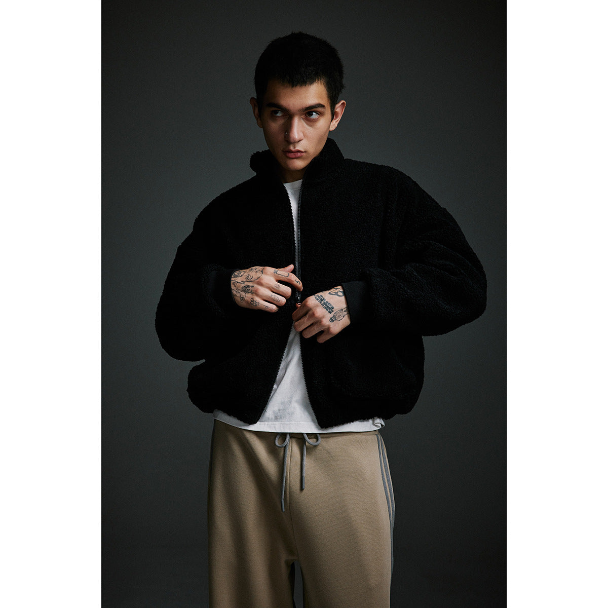 Model wearing a black zip-up fleece jacket over a white shirt with tan drawstring pants.