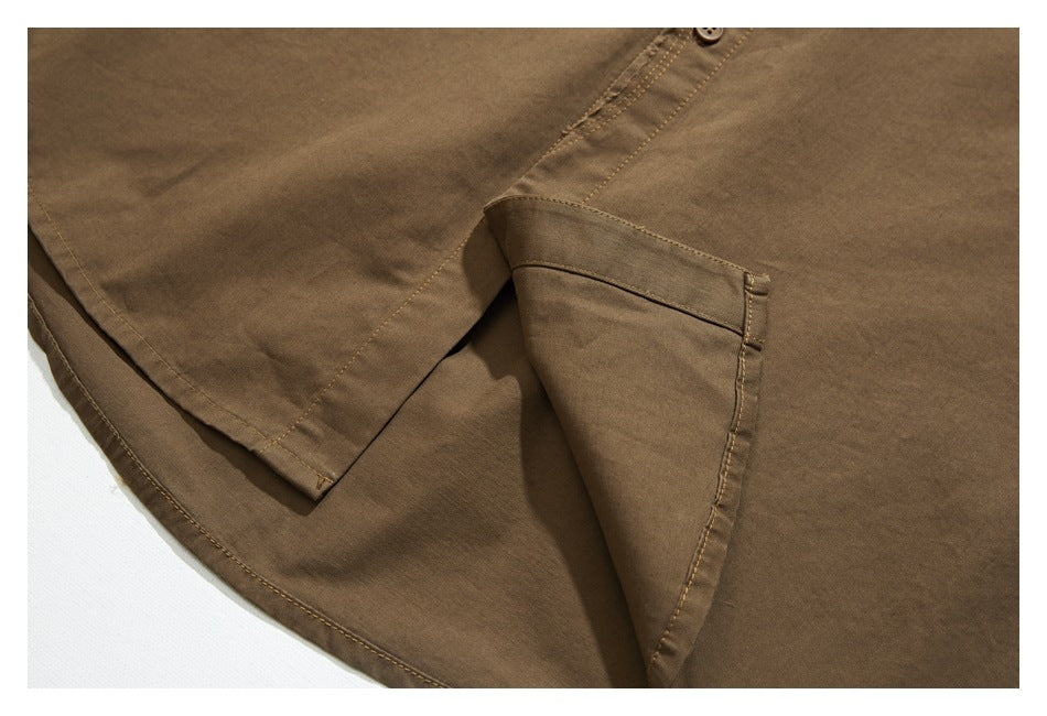 Close-up of a brown shirt's side opening and layered hem, showing stitched edges and a button.