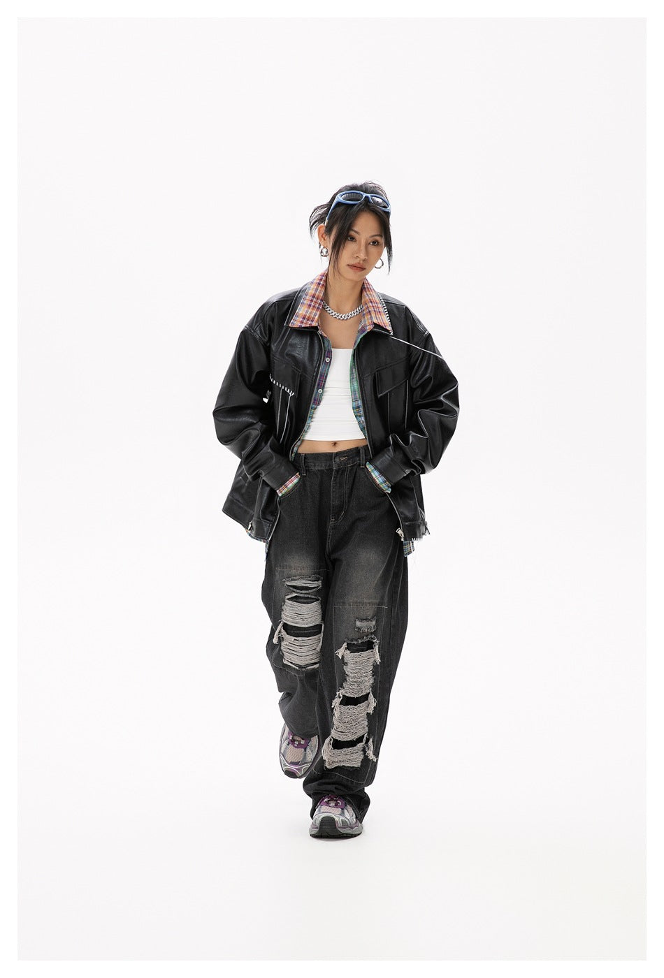 Model wearing a black jacket with colorful plaid accents, a white crop top, and distressed black jeans.