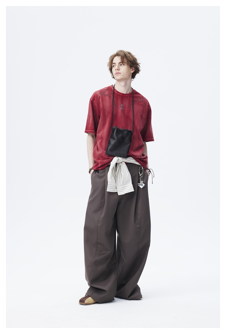 Model turned to the side in the red distressed T-shirt, wide brown trousers and black crossbody pouch