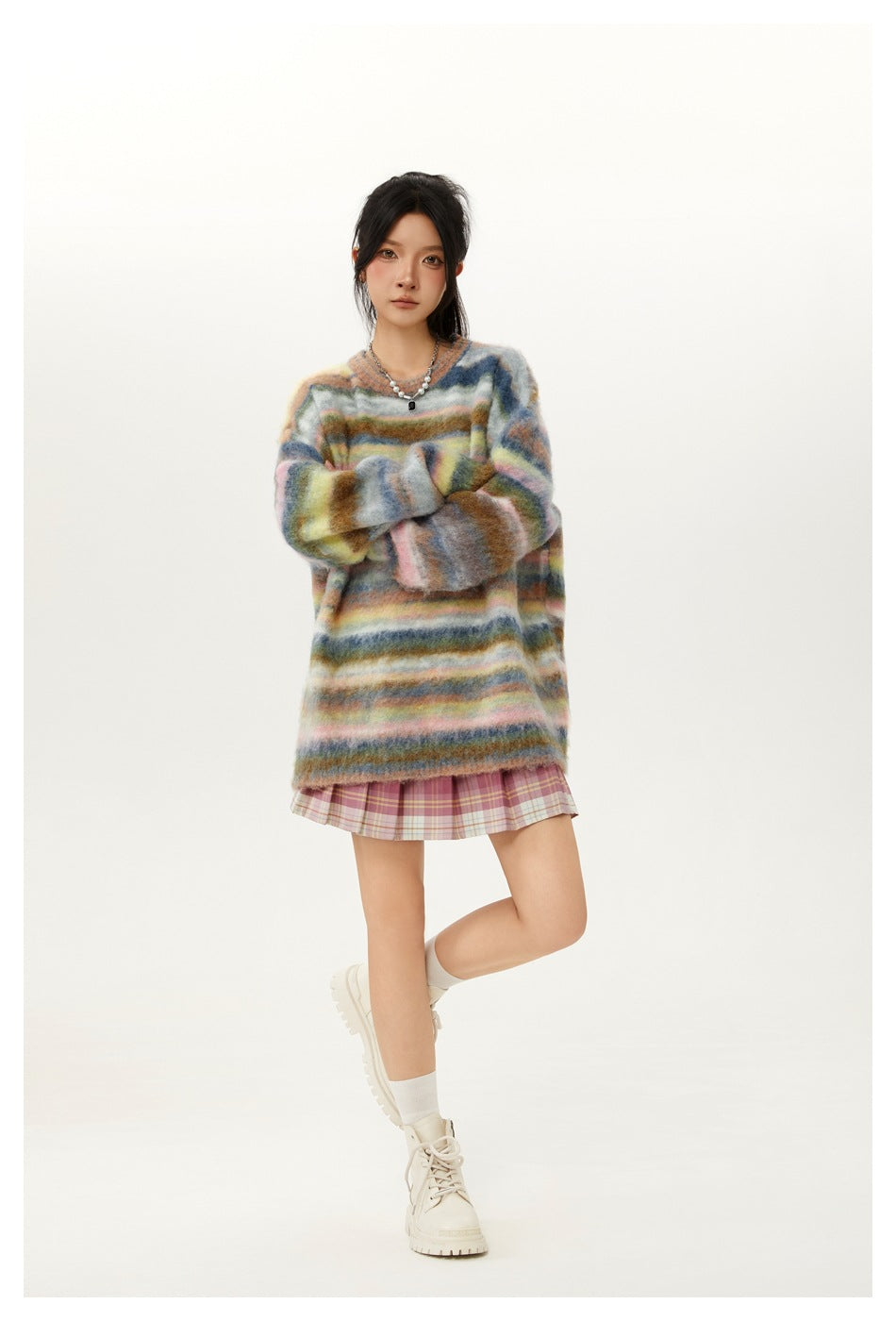 Model poses in an oversized fuzzy multicolor striped sweater, pink plaid skirt, white socks and boots.