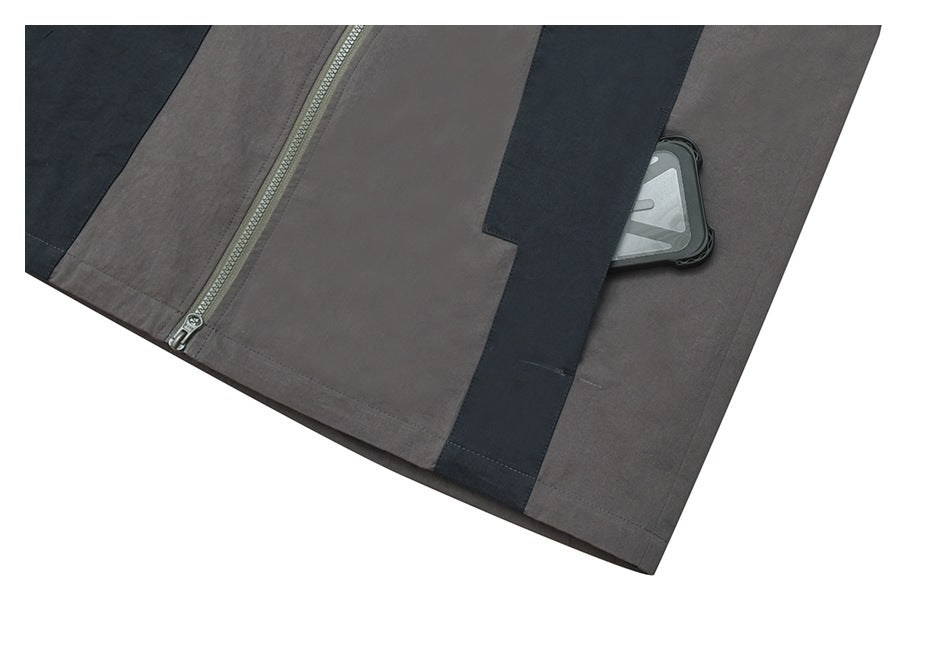 Close-up of a charcoal jacket with dark contrast panels, a zipper, and a pocket holding a small device.