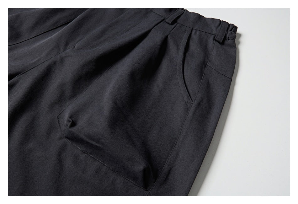 Close-up of charcoal trousers showing a curved side pocket, front pleat, and waistband with belt loops.
