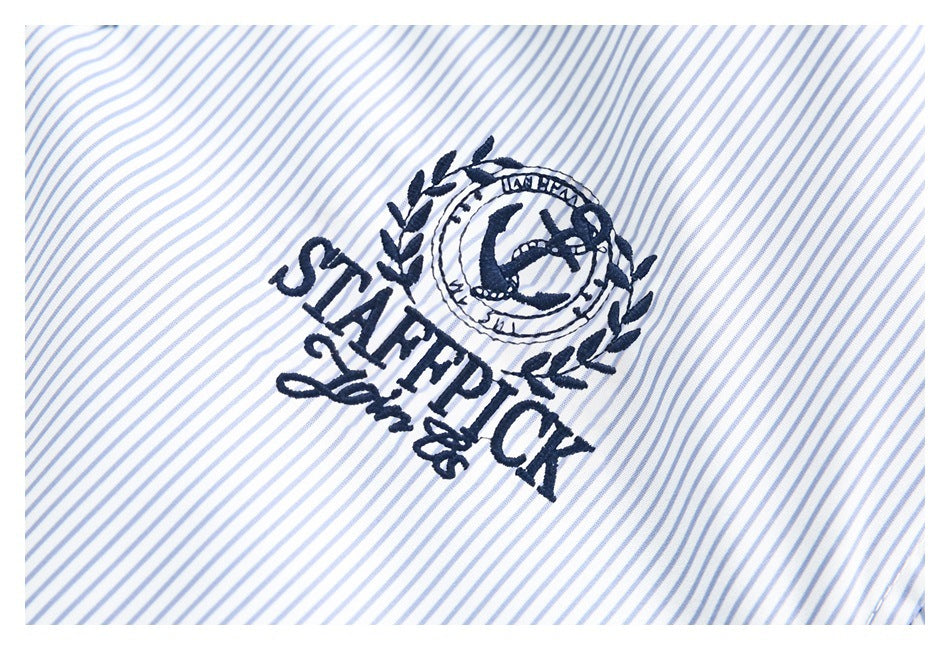 Close-up of a navy embroidered crest and lettering on white fabric with thin blue stripes.