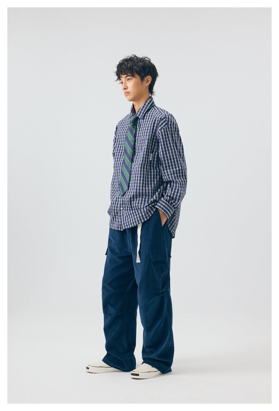 Side view of model in deep blue wide-leg cargo pants with a white belt, plaid shirt, striped tie and sneakers