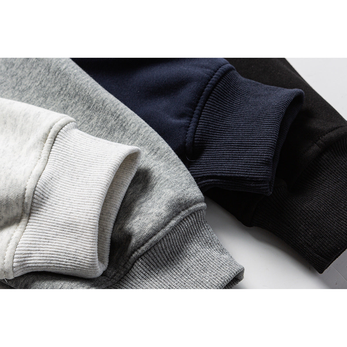 Close-up of ribbed cuffs on folded hoodies in white, heather gray, navy, and black.