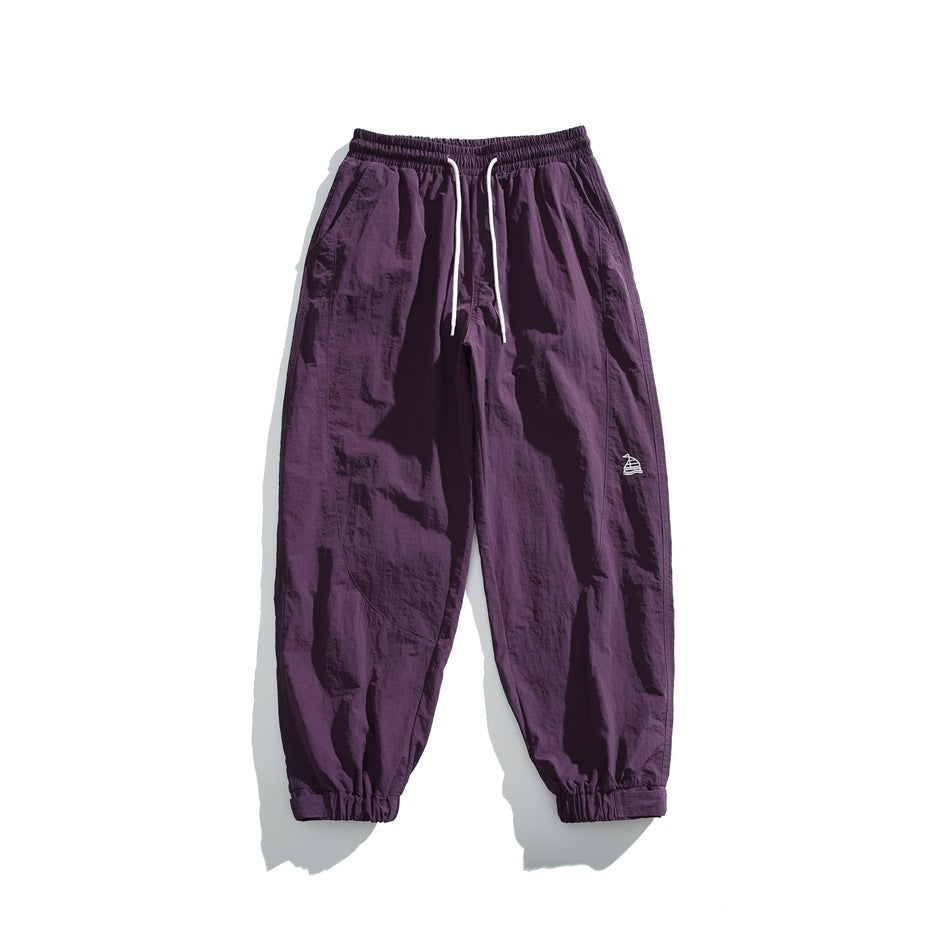 Purple jogger pants flat lay with white drawstring, elastic cuffs and small embroidered logo