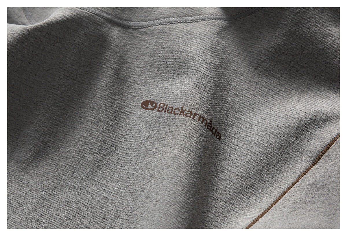 Close-up of a gray garment panel with a small brown Blackmamba logo and contrast stitching.