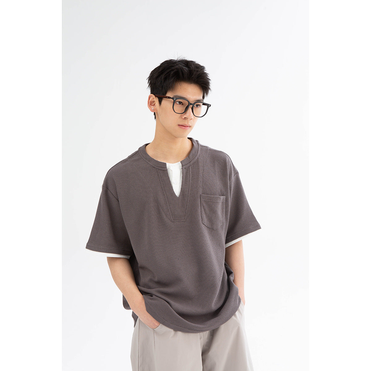 Close view of a model wearing a charcoal-gray textured short-sleeve shirt with a white split-neck inset and chest pocket.